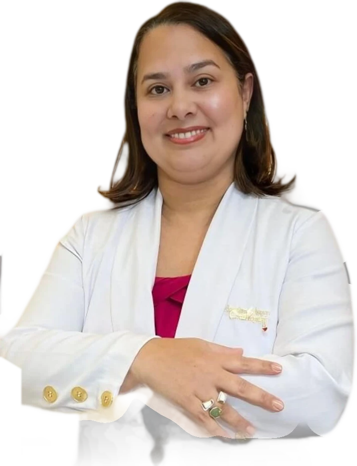 Dra. Sueleny Vinson, de jaleco branco com botões dourados e blusa magenta, braços cruzados, sorrindo.